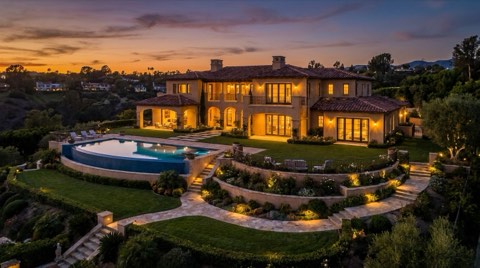 A grand estate home exterior with manicured grounds and soft landscape lighting glowing at dusk