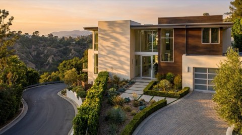 A staged luxury hillside home exterior in golden hour light with a curved driveway and manicured landscaping