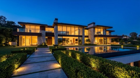A dramatically lit Bel Air estate exterior at blue hour with warm interior lights glowing through large windows