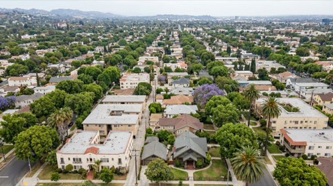 An elevated view of a Los Angeles residential neighborhood grid with tree canopy over a mix of apartment buildings and homes