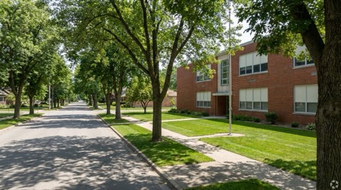 A generic brick elementary school building exterior with a trimmed lawn and tree shadows in midday light