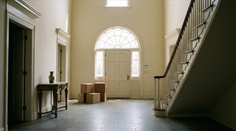 An elegant, mostly empty estate foyer with a few neatly stacked moving boxes near the entrance