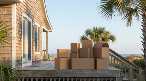 Cardboard moving boxes stacked on a coastal home porch in morning light