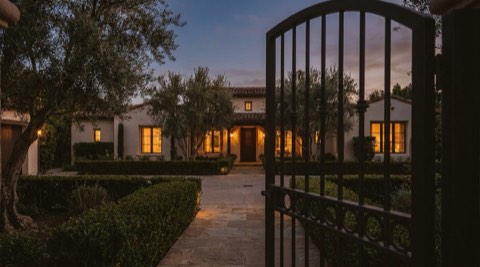 Wrought-iron gate ajar in front of a quiet elegant home at dusk