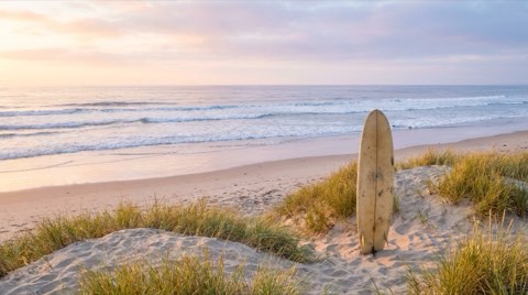 A quiet, uncrowded beach at sunrise with a surfboard resting upright in the sand