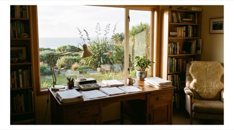 A cozy home office desk near a window overlooking a coastal garden in warm natural light