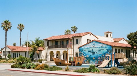 A cheerful elementary school exterior with a playground and palm trees under a clear sky