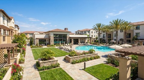 A landscaped condo courtyard with a resort-style pool and clubhouse building as a shared community amenity under bright daylight.