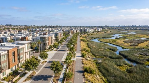 Elevated view of Playa Vista showing modern condo buildings on one side transitioning into open wetland marsh greenery on the other, marking the edge between neighborhood sub-areas.