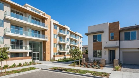 A modern multi-unit apartment building with a shared entrance standing near a smaller private townhome, both in matching contemporary style under bright daylight.