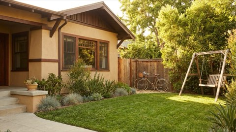 A traditional Beverlywood home's front yard with bicycles and a swing set in bright daytime light