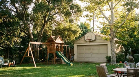 A Los Feliz family backyard with a swing set, grassy lawn, and mature shade trees in bright afternoon light