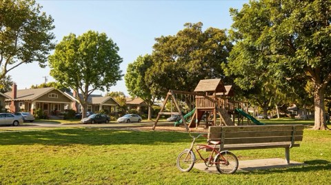 A neighborhood park in Santa Monica with a wooden playground structure, shade trees, and a child's bicycle resting against a bench