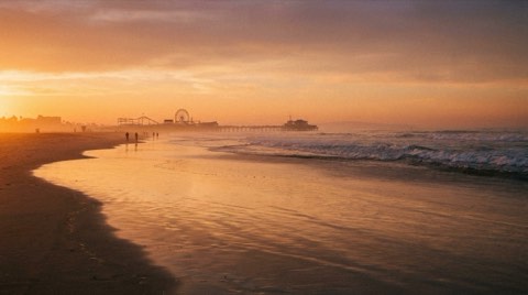 The Santa Monica coastline at golden hour with the pier and Ferris wheel silhouetted in the distance along the curving sandy beach
