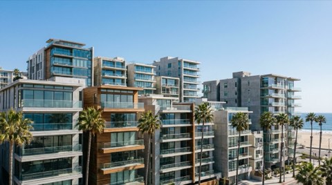 Dense modern mid-rise condo buildings near the beach in Santa Monica with glass balconies, seen from a low angle against a clear blue sky
