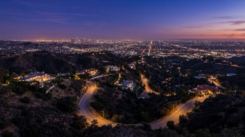 A sweeping blue-hour vista of scattered hillside homes with glowing windows across the Hollywood Hills canyons above the distant city lights
