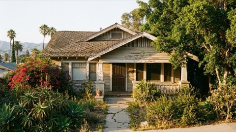 A slightly weathered traditional home exterior with mature, overgrown landscaping suggesting long ownership.