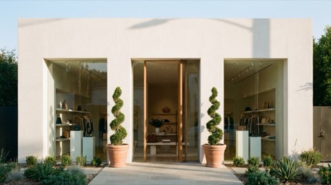 An upscale boutique storefront with a minimalist glass facade and potted topiary trees flanking the entrance