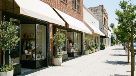 A retail storefront streetscape with clean awnings, display windows, and a wide sidewalk in bright midday light