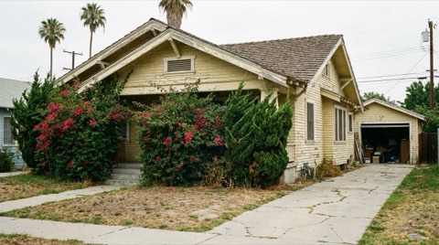 An older home exterior in need of updating, with faded paint and an overgrown front yard