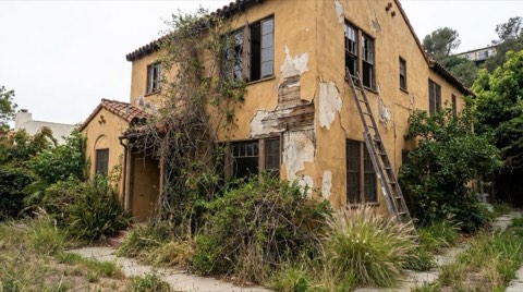 An older Los Feliz home in need of renovation with faded paint and an overgrown yard under overcast midday light