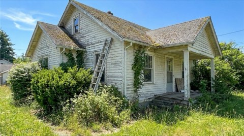 An older single-family home exterior with weathered paint and a ladder leaning against the side wall in clear midday light