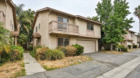 A modest condo exterior with faded paint and overgrown landscaping suggesting renovation potential, under neutral daylight.
