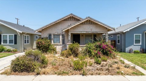 An older fixer-upper home exterior with dated paint and an overgrown yard needing work.