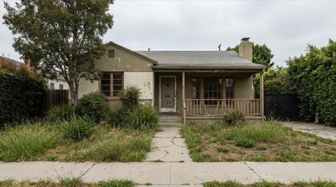 A weathered 1940s single-family home in Westwood with faded paint, an overgrown front yard, and a sagging porch railing, photographed straight-on under flat overcast light