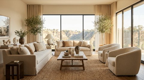 A warm, bright staged living room interior with neutral furniture and natural light through large windows