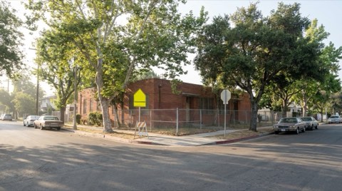 A residential street near an elementary school with a low brick building visible over a fence in morning light.