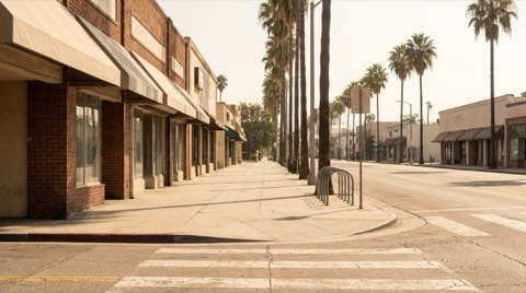 A wide sidewalk on a small-town commercial street with a bicycle rack and storefronts under palm trees.