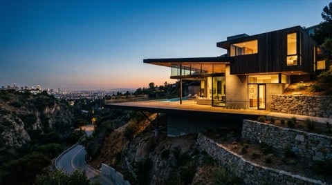 A modern glass-walled Los Feliz hillside home with a cantilevered deck overlooking a canyon view at dusk
