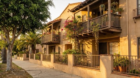 Low-rise apartment facade with balconies on a tree-lined LA sidewalk
