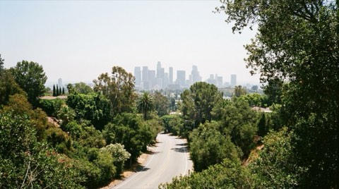 A winding hillside road descending toward a distant hazy skyline of office towers