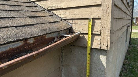 A close detail shot of a home's roofline, gutter, and foundation corner during an inspection