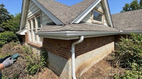 A close-up exterior detail of a single-family home showing the roofline, windows, and foundation area in bright midday light