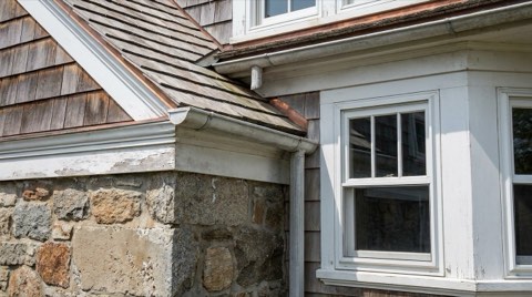A close-up architectural detail of a coastal home's foundation, roofline, and window trim