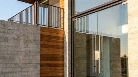 Close-up of a modern condo building entrance showing glass doors, balcony railing details, and contemporary building materials in bright daylight.