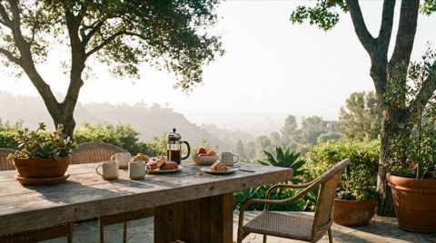 A terrace breakfast table set with coffee cups overlooking a hazy Bel Air canyon in soft morning light