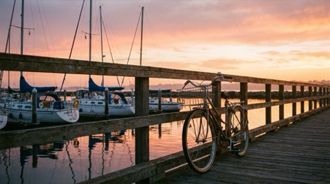 A relaxed sunset over a quiet marina boardwalk with sailboats and a bicycle by the railing
