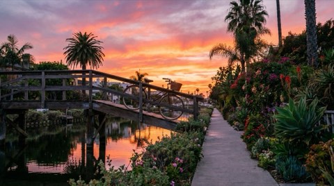 A relaxed sunset scene along the Venice canal boardwalk with a bicycle by a footbridge