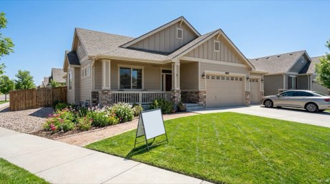 A single-family home exterior with a blank sign frame near the sidewalk and a tidy front yard in bright midday light