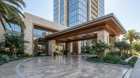 The covered porte-cochere entrance drive of a full-service high-rise condominium tower, with polished stone paving and manicured landscaping under clear midday light.